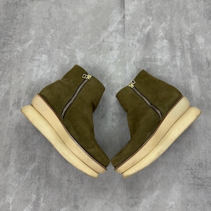 May include: A pair of olive green suede ankle boots with a cream-colored platform sole. The boots have a side zipper with a gold-colored zipper pull. The boots are displayed on a gray background.
