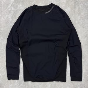 Puede incluir: Camiseta deportiva negra de manga larga con la palabra "SPECIALIZED" impresa en gris en el cuello. La camiseta tiene cuello redondo y está hecha de un material elástico y transpirable. Diseñada para actividades deportivas.