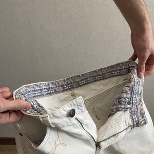 May include: White denim jeans with a patterned waistband. The waistband is turned inside out to show the pattern.