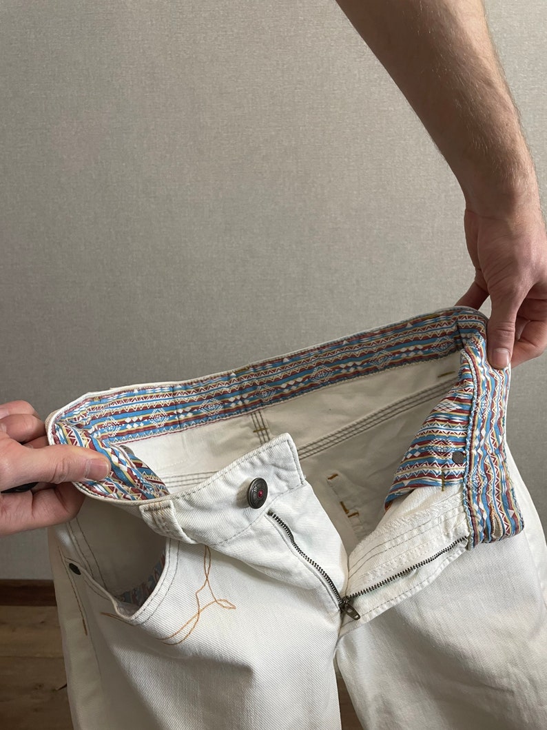 May include: White denim jeans with a patterned waistband. The waistband is turned inside out to show the pattern.