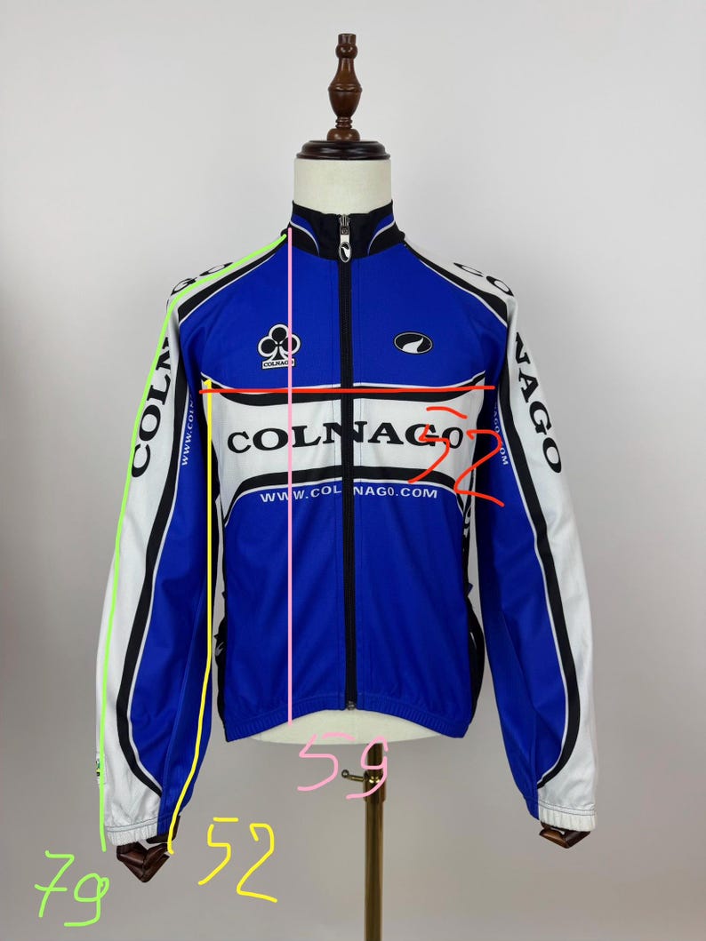 May include: A blue, white, and black Colnago cycling jacket with a full zipper. The jacket features the Colnago logo and website address. The jacket's measurements are 79 inches in length, 52 inches in the chest, and 59 inches in the waist.