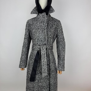 Peut inclure: Un manteau à motif chevrons noir et blanc avec une capuche noire et une ceinture assortie. Le manteau a un design classique avec un col et des manches longues. Le manteau est présenté sur un mannequin.