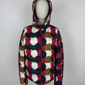 May include: A patterned puffer jacket with a hood. The jacket has a red zip and is decorated with a polka-dot design in white, red, navy, green, and brown. The jacket is displayed on a mannequin.
