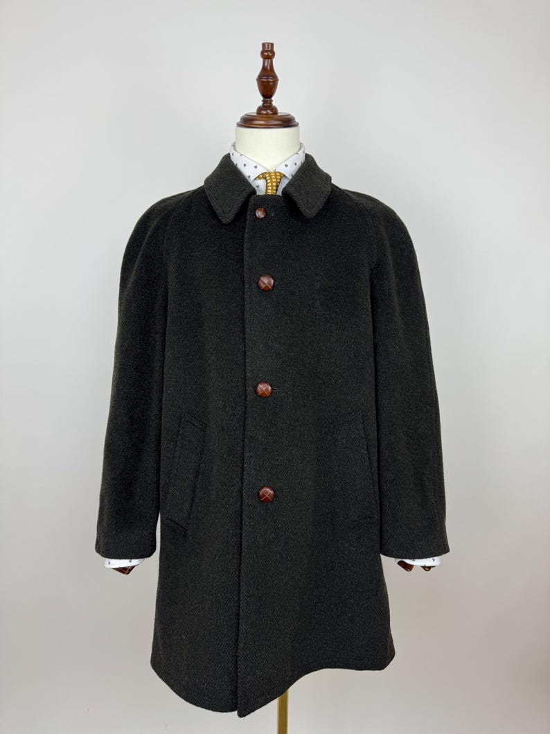 May include: A dark brown wool coat with a classic design. The coat features a notched collar, three brown buttons, and two front pockets. The coat is displayed on a mannequin.
