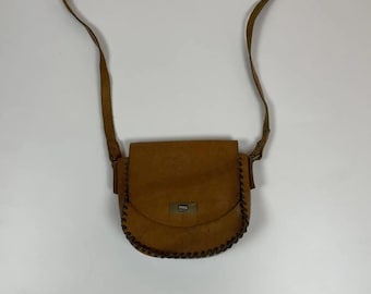 May include: A brown leather crossbody bag with a flap closure and a stitched detail around the edges. The bag has a long adjustable strap.