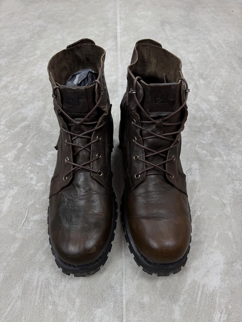 May include: A pair of brown leather work boots with a lace-up design. The boots have a rugged, worn appearance, with visible stitching and a thick, textured sole. The boots are a classic style, suitable for various outdoor activities.