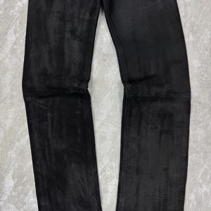 May include: A pair of black leather trousers featuring a matte finish with visible tonal variations and horizontal seam detailing across the mid-thigh area. The trousers have a straight-leg cut with a clean hem and a structured, multi-panel construction.