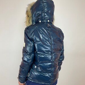 Puede incluir: Una chaqueta acolchada azul marino con capucha forrada de piel. La chaqueta tiene un acabado brillante, casi mojado.