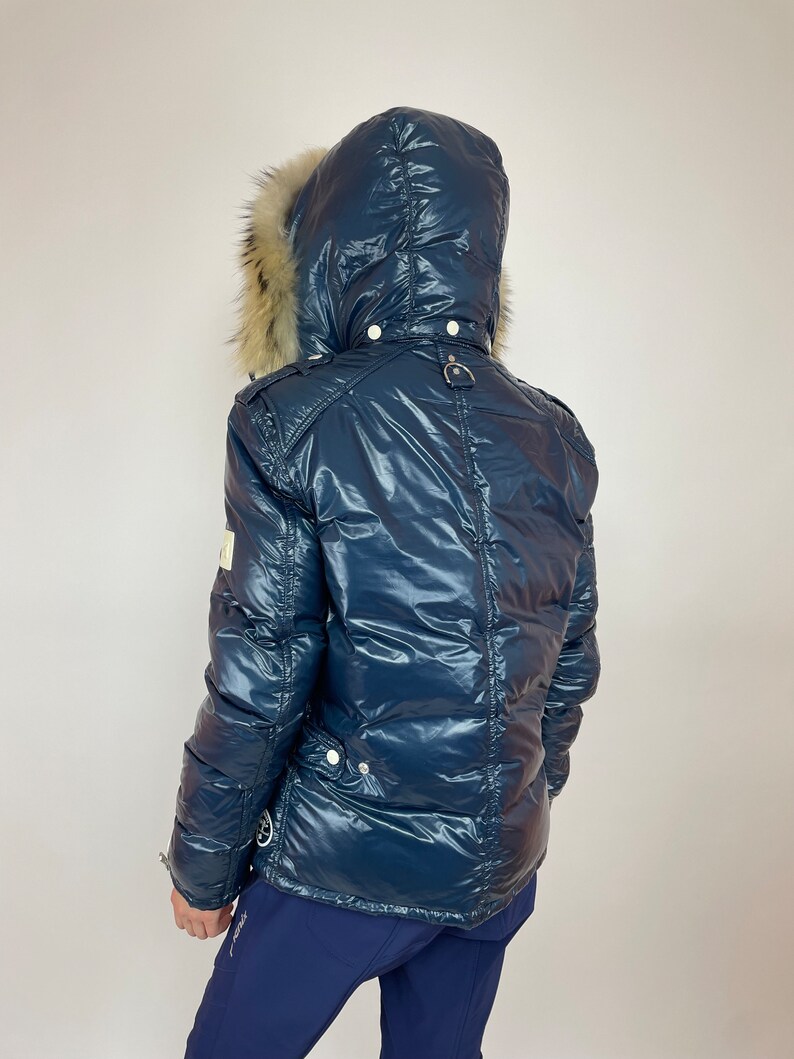 Puede incluir: Una chaqueta acolchada azul marino con capucha forrada de piel. La chaqueta tiene un acabado brillante, casi mojado.