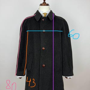 May include: A dark gray wool coat with a classic design. The coat features a notched collar, button closure, and two front pockets. The coat's length is approximately 38 inches, with a sleeve length of 24 inches. The chest measures 43 inches, and the shoulders are 24 inches.