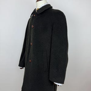 May include: A dark green wool coat with a classic design. The coat features a notched collar, three brown buttons, and two front pockets. The sleeves have white cuffs. The coat is displayed on a mannequin.