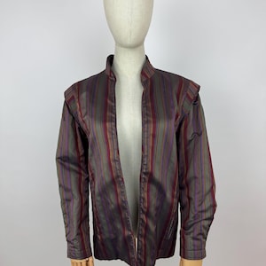 May include: A striped jacket in shades of burgundy, purple, and olive green. The jacket has a mandarin collar and long sleeves. The fabric has a subtle sheen, and the jacket is displayed on a mannequin.