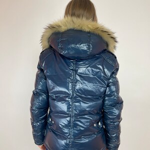 Puede incluir: Una chaqueta acolchada azul marino con capucha de piel sint&eacute;tica. La chaqueta tiene un aspecto brillante, casi mojado.
