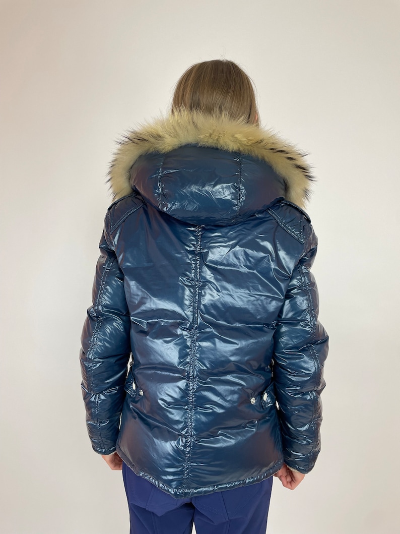 Puede incluir: Una chaqueta acolchada azul marino con capucha de piel sint&eacute;tica. La chaqueta tiene un aspecto brillante, casi mojado.