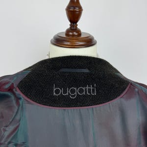 May include: Close-up of the inside of a dark brown wool coat with the brand name "bugatti" embroidered in silver thread on the collar. The lining is a shimmering, iridescent fabric with shades of purple, teal, and gray.