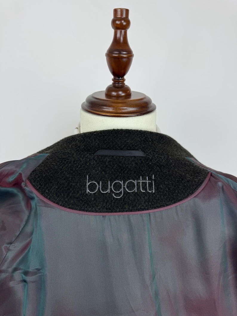 May include: Close-up of the inside of a dark brown wool coat with the brand name "bugatti" embroidered in silver thread on the collar. The lining is a shimmering, iridescent fabric with shades of purple, teal, and gray.