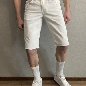 May include: White denim shorts with frayed hems and a brown leather belt. The shorts have a relaxed fit and are worn with white socks and white sneakers.