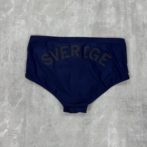 May include: Navy blue swim briefs with the word "SVERIGE" printed across the back in dark green. The swimwear is a solid color and appears to be made of a smooth, possibly synthetic material. The briefs have a classic, brief cut.