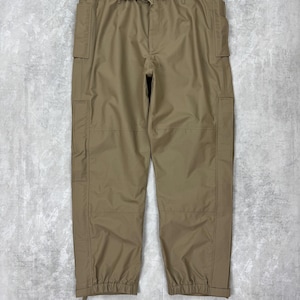 May include: Khaki cargo trousers featuring multiple pockets and a drawstring waist. The trousers have a relaxed fit and elasticated cuffs at the ankles. The fabric appears to be a lightweight, durable material.
