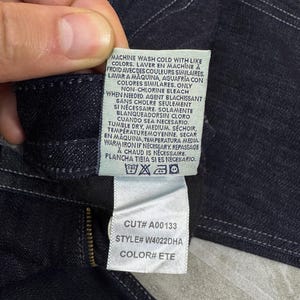 Puede incluir: Una prenda de mezclilla azul oscuro con una etiqueta de cuidado blanca con texto en negro. La etiqueta incluye instrucciones de lavado, n&uacute;mero de corte A00133, n&uacute;mero de estilo W4022DHA y c&oacute;digo de color ETE. Costuras blancas visibles.