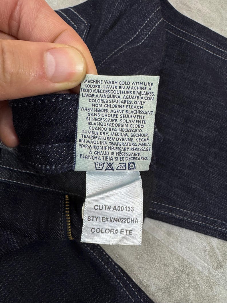 Puede incluir: Una prenda de mezclilla azul oscuro con una etiqueta de cuidado blanca con texto en negro. La etiqueta incluye instrucciones de lavado, n&uacute;mero de corte A00133, n&uacute;mero de estilo W4022DHA y c&oacute;digo de color ETE. Costuras blancas visibles.