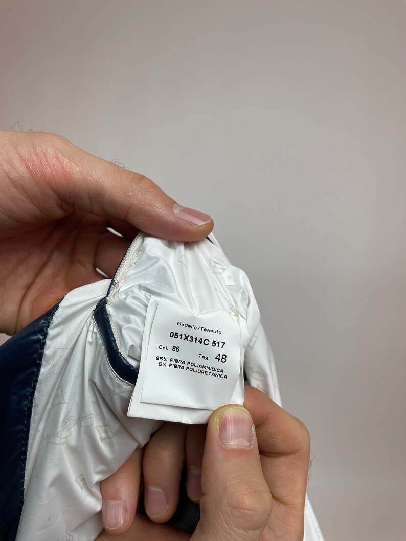 Puede incluir: Etiqueta blanca con texto negro, que muestra el n&uacute;mero de modelo 051X314C 517, el color 86 y la talla de la etiqueta 48. La etiqueta tambi&eacute;n indica la composici&oacute;n de la tela como 95% poliamida y 5% poliuretano.
