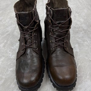 May include: A pair of brown leather work boots with a lace-up design. The boots have a rugged, worn appearance, with visible stitching and a thick, textured sole. The CAT logo is visible on the tongue of the boots.