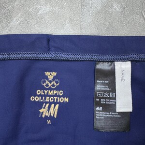 May include: Navy blue athletic wear with gold text reading "OLYMPIC COLLECTION" and the H&M logo. A tag indicates the item is made in Italy and lists the materials as 80% Polyamid and 20% Elastan. The size is medium.