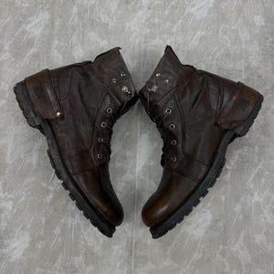 May include: A pair of brown leather boots with laces and metal accents. The boots have a rugged, worn appearance, with visible stitching and a thick, textured sole. The boots are designed for durability and style.