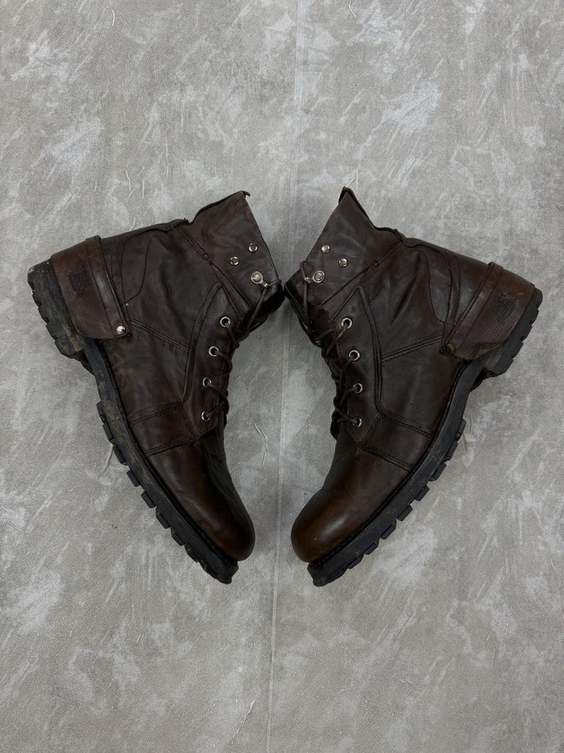 May include: A pair of brown leather boots with laces and metal accents. The boots have a rugged, worn appearance, with visible stitching and a thick, textured sole. The boots are designed for durability and style.