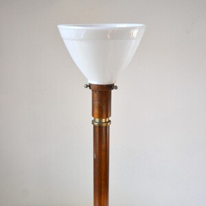 May include: A tall, copper floor lamp with a white glass shade. The lamp has a simple, cylindrical design with a round base.