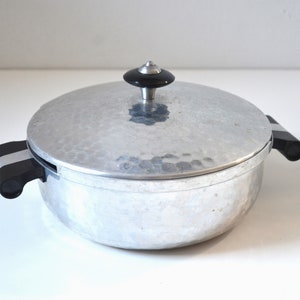 May include: A silver aluminum pot with a hammered finish and black plastic handles. The pot has a lid with a black knob.