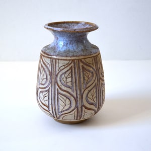 May include: A small, brown and white ceramic vase with a blue glaze on the top. The vase has a leaf pattern carved into the surface.