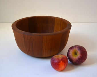 May include: A large, wooden bowl made of dark brown wood with two red apples sitting in front of it.