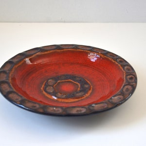 May include: A red ceramic bowl with a brown rim and a textured design. The bowl has a glossy finish and is perfect for serving snacks or dips.