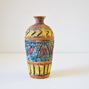 May include: A small, brown ceramic vase with a geometric design in yellow, blue, red, and green. The vase has a narrow neck and a rounded body.