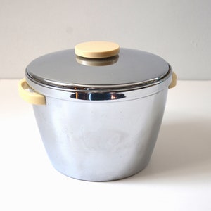 May include: A chrome ice bucket with a lid and two handles. The lid has a cream-colored knob.