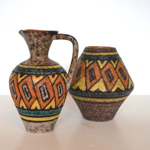 May include: Two ceramic vases with geometric patterns. One is a pitcher with a handle, the other is a rounded vase. Both have orange, yellow, and teal diamond designs on a textured brown background.