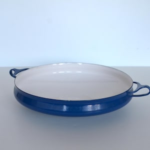 May include: A round, blue and white enamelware pan with two loop handles. The pan has a white interior and a glossy blue exterior. This kitchenware is suitable for cooking and serving.