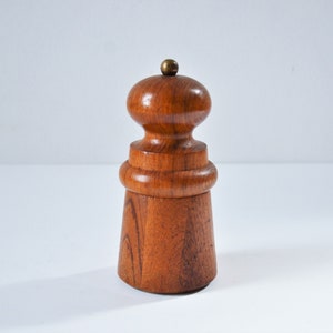 May include: A wooden salt and pepper grinder with a brass top. The grinder is made of dark brown wood with a natural grain pattern.