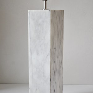 Puede incluir: Una base de l&aacute;mpara de m&aacute;rmol blanco con una toma de l&aacute;mpara plateada y un interruptor negro. La base es rectangular y tiene un acabado liso y pulido.