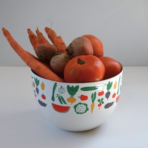 Puede incluir: Un cuenco de cerámica blanco decorado con un patrón colorido de varias verduras y frutas, lleno de zanahorias naranjas frescas, remolachas redondas marrones y tomates rojos brillantes. El cuenco presenta ilustraciones de sandía, coliflor y pimientos.