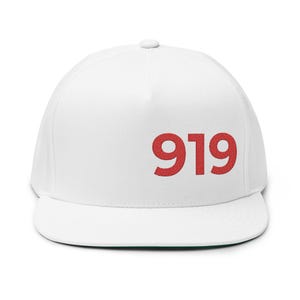 Może przedstawiać: Biała czapka z daszkiem z płaskim daszkiem, z wyszytym czerwonym numerem "919". Czapka ma strukturalny krój i zakrzywiony daszek z zielonym spodem. Klasyczny dodatek.