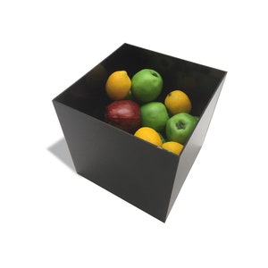 May include: A black square container filled with a variety of fruit, including green apples, yellow lemons, and a red apple.