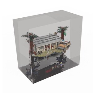 May include: A clear acrylic display case with a black base, showcasing a LEGO Stranger Things set featuring the Byers house, a car, and minifigures. The set is suspended in mid-air, creating a floating effect.