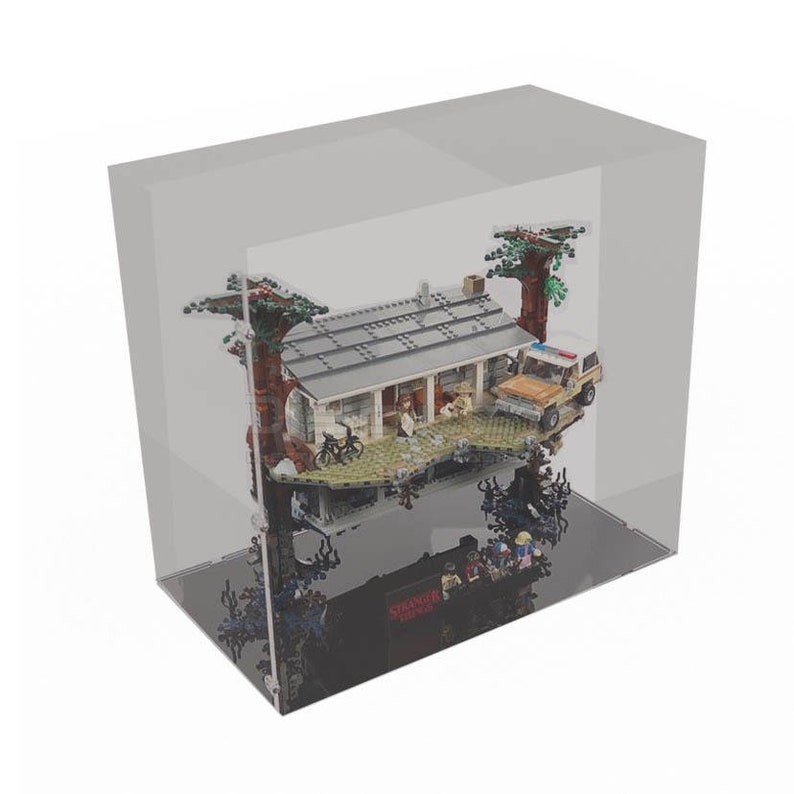 May include: A clear acrylic display case with a black base, showcasing a LEGO Stranger Things set featuring the Byers house, a car, and minifigures. The set is suspended in mid-air, creating a floating effect.
