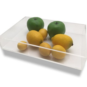 May include: A clear acrylic rectangular tray filled with green apples and yellow lemons. The tray is sitting on a white surface.