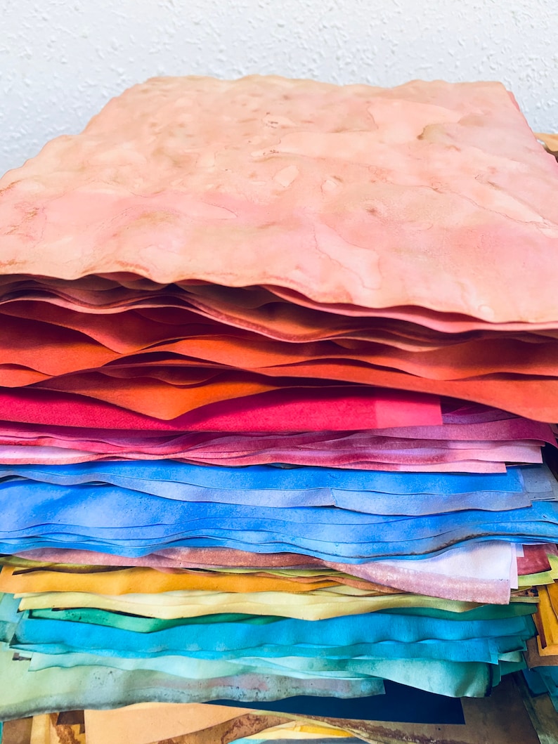 May include: A stack of handmade paper in various shades of pink, orange, blue, green, and yellow. The paper is layered and textured, creating a unique and artistic look.
