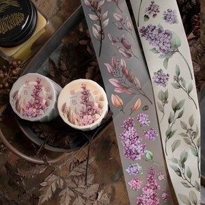 May include: Washi tape rolls and strips with floral designs in purple, pink, and green. The tape rolls have text in a foreign language. The strips showcase botanical illustrations of leaves and flowers.