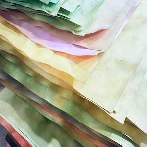 May include: A stack of colorful paper sheets in various shades of green, yellow, pink, and white. The paper is slightly textured and has a vintage look.